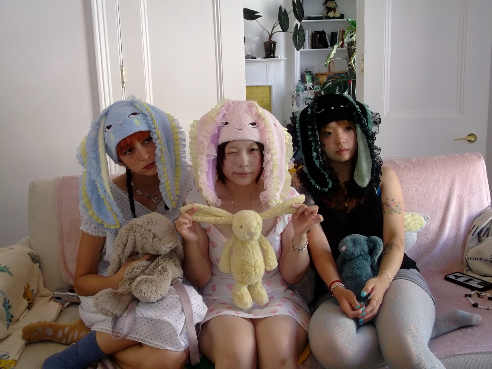 Three models wearing HOHOMIE bunny caps on a couch