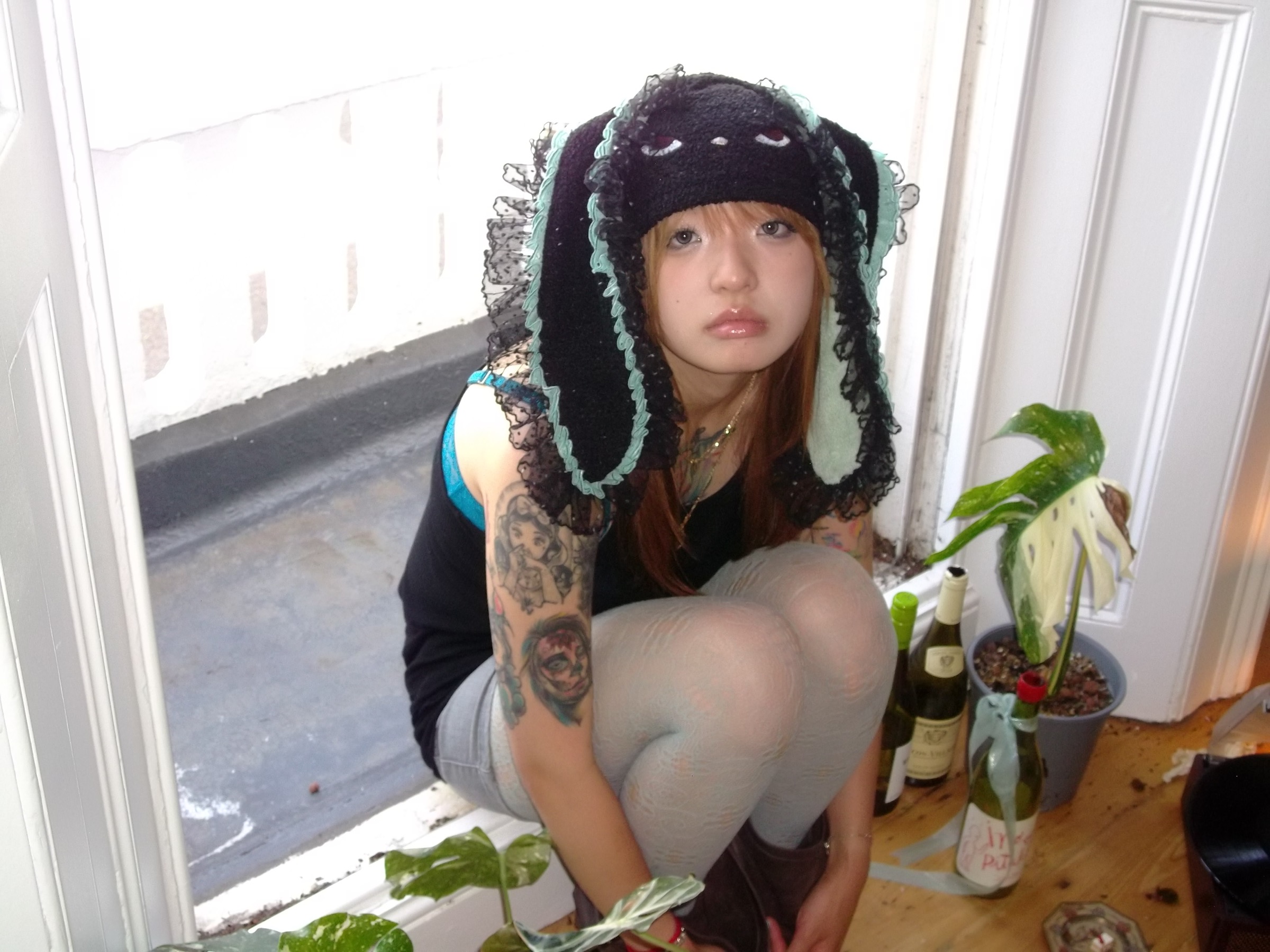 Model wearing the black HOHOMIE Naughty Bunny Hood with mint trim and lace ruffles by a bright window
